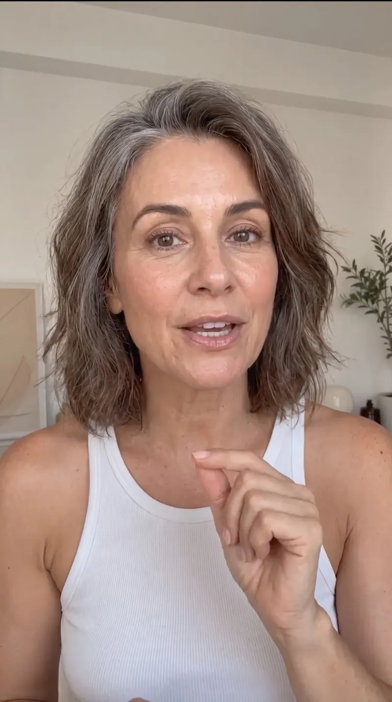 Imagem feita com Nano Banana Pro: selfie estilo UGC de uma mulher de uns 50 anos com cabelo grisalho falando para a câmera em casa